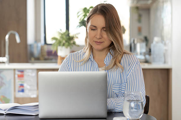 istock Young woman working remotely on laptop in modern kitchen setting 2205507304