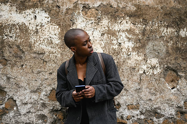 istock Young woman looking over shoulder while using phone in front of old wall 2205507874