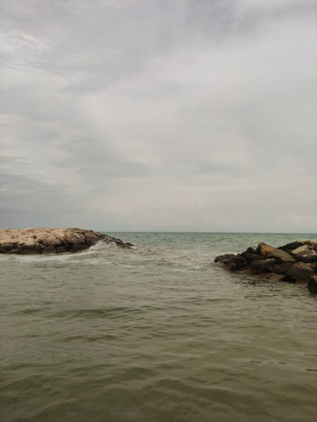 Foamy waves pounding rocky breakwaters under gray skies, revealing dramatic coastal landscape near bibione, italy