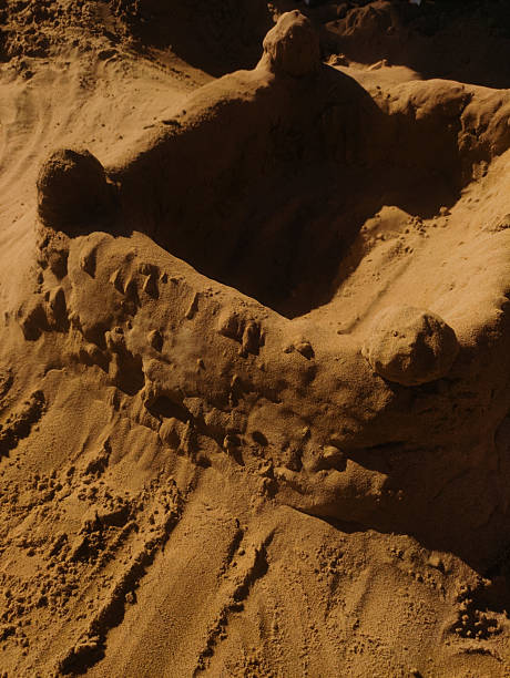 A sandcastle washes away with the waves under the evening sun.