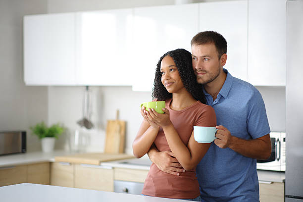 istock Interracial couple drinking looking away in an kitchen 2205518793
