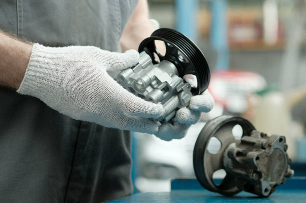 istock Car service. An auto mechanic is preparing to replace the hydraulic power steering pump. A new rotary oil pump is in the hands of an auto mechanic. There is a faulty pump on the worktable. 2205520044