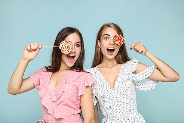 istock Young happy girlfriends with sweet lollipops on blue background 2205522226
