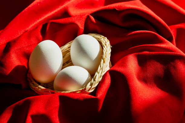 A gift basket with three chicken eggs on bright red fabric in sunlight, resembling an expensive gift, highlighting the price of chicken eggs, the luxury of ordinary food products, and the rising cost of food.