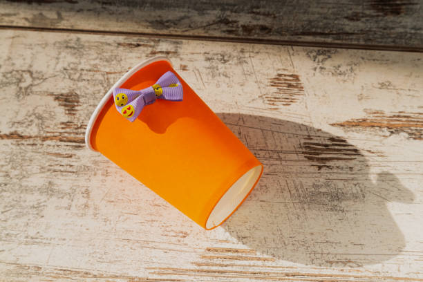 A cheerful ribbon on a paper orange disposable cup in sunlight on a table. The lightness of celebration, corporate festivity, and preparation for a party.