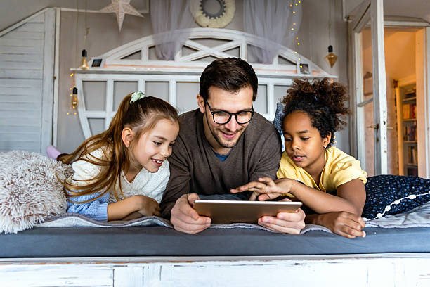 istock Happy diverse family resting at home on bed spending time together and using digital gadgets. 2205525208