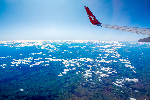 Melbourne, Australia - Sep 3, 2022: Qantas Flying Kangaroo Corporate Logo on aircraft wingtip. Flying above fluffy white clouds with blue sky. Plane holds steady to reveal the farming pastures below.