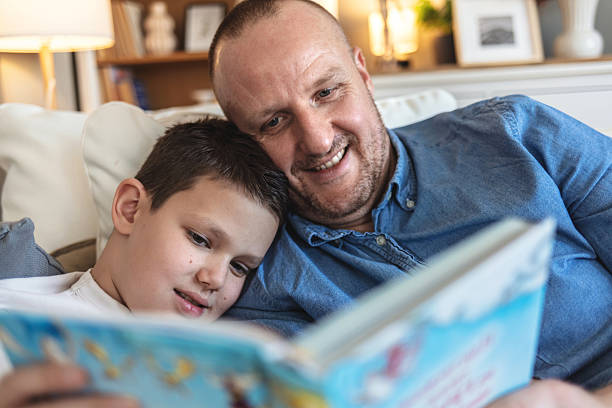 istock Father and son read a book and have fun while spend time together. Happy father and son reading interesting book and relaxing together at home. 2205525699