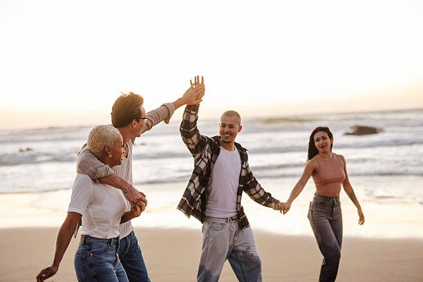 istock Happy friends giving high five and holding hands while walking on the beach 2205525769