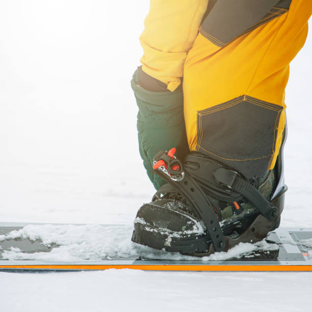istock snowboarder on high mountain at ski resort preparing for freeride fastens strap on binding, close-up at sunset 2205527820