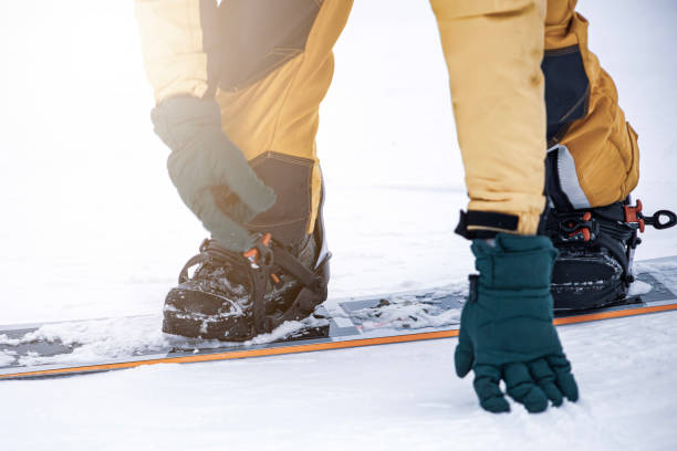 istock snowboarder on high mountain at ski resort preparing for freeride fastens strap on binding, close-up at sunset 2205527822