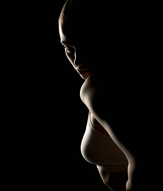 istock Mysterious side profile of a woman in low-key lighting. Shadows obscure most features, highlighting contours. Evokes silence and intrigue. Dark background 2205530488