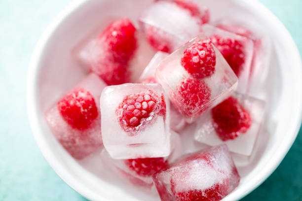 istock Frozen ice cubes with fresh raspberries in a white bowl. Blue background. Close up. 2205532970