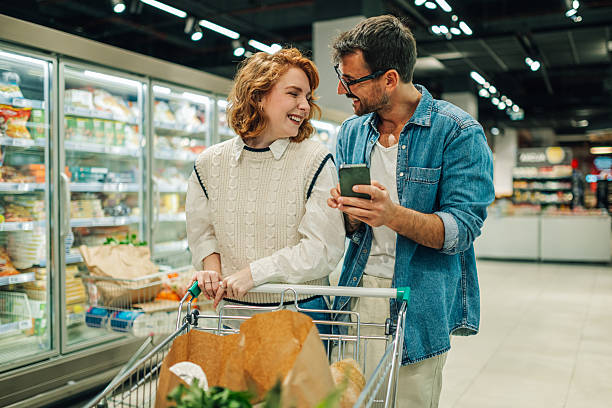 istock Couple using smartphone while shopping groceries at supermarket 2205533185
