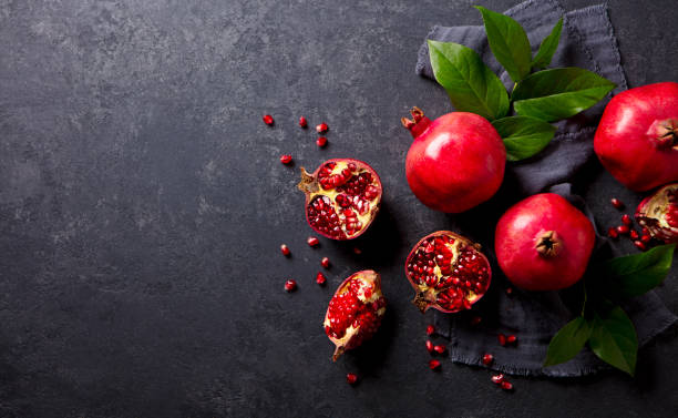 istock Fresh pomegranates with green leaves on the table. Dark grey background. Copy space. Top view. 2205533887