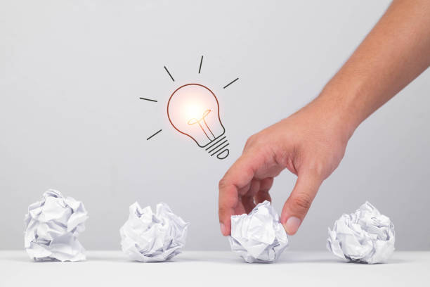 istock A hand selecting a crumpled paper ball with a glowing light bulb above, symbolizing the moment of creative insight or inspiration. 2205534965
