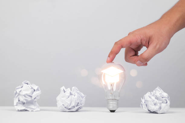 istock A hand touching a glowing light bulb surrounded by crumpled paper, symbolizing creativity and the birth of ideas. 2205534975