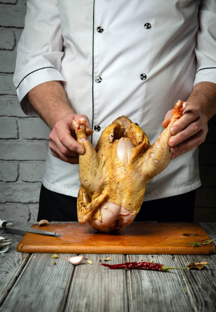 istock A skilled chef holds a whole chicken upside down, ready for preparation. The rustic wooden surface and textured wall add character to the culinary atmosphere, highlighting the art of cooking 2205537440