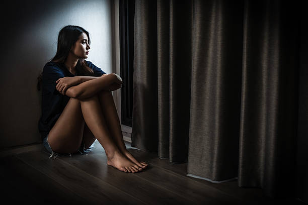 istock young woman sitting alone in dimly lit room, reflecting on her thoughts. atmosphere conveys sense of solitude and introspection 2205540241