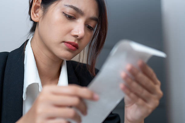 woman in black blazer examines receipt with focused expression, reflecting on her finances. Her serious demeanor suggests concern or contemplation