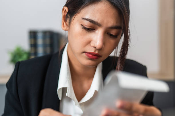 woman in black blazer examines receipt with focused expression, reflecting on her finances. Her serious demeanor suggests concern or contemplation