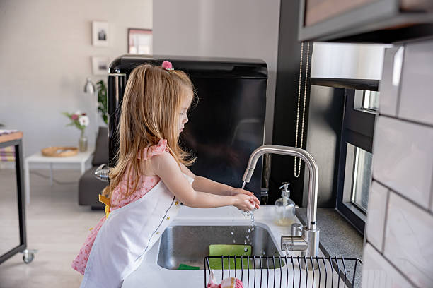 istock A young girl wearing an apron washes her hands at the kitchen sink, practicing hygiene and cleanliness in a bright, modern home. 2205541097