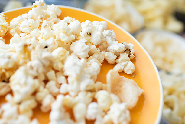 popcorn on a plate, plate on the background of bowls with various snacks on the table