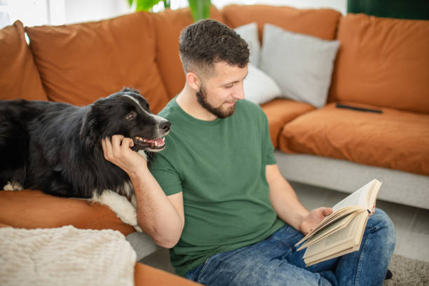 istock Young man relaxes with his dog while reading a book in a cozy living room setting 2205545505
