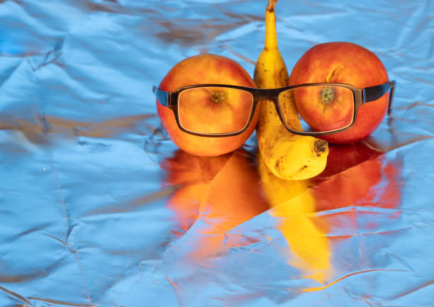 Two apples alongside a banana that is humorously wearing glasses, all placed on a bright blue surface, creating an amusing visual scene