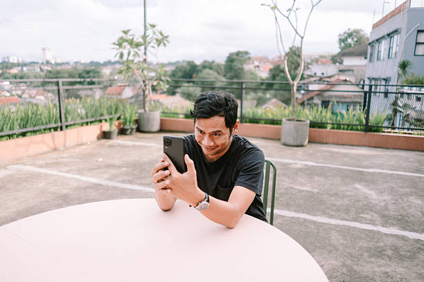 istock Smiling Man Taking Selfie on Rooftop with Urban Panorama Behind 2205549766