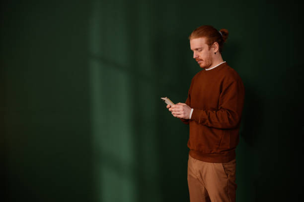 istock Young adult man using smartphone on green background with window light reflection 2205559315