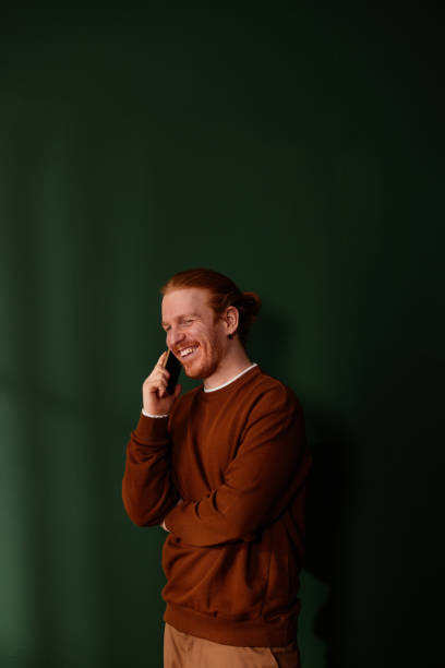 istock Young redhead man laughing while talking on phone near green wall 2205559334