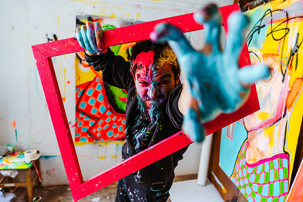 istock Expressive Artist Holding a Red Frame with Painted Hands. 2205559451