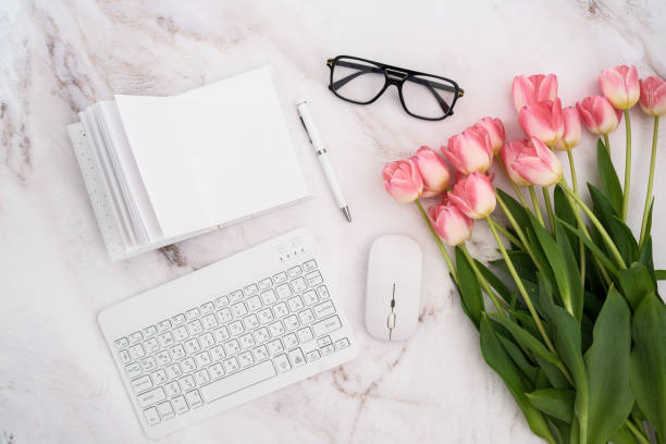 A stylish and modern workspace featuring a sleek keyboard, a mouse, fresh flowers, and elegant glasses.