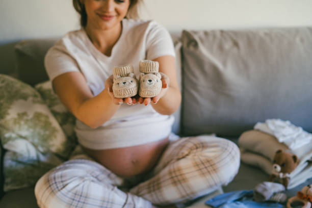 Young beautiful woman in pajamas is packing bag of baby things for the maternity ward. Model with belly is preparing to be mother.