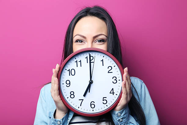 istock Young woman holding a clock on pink background 2205572912