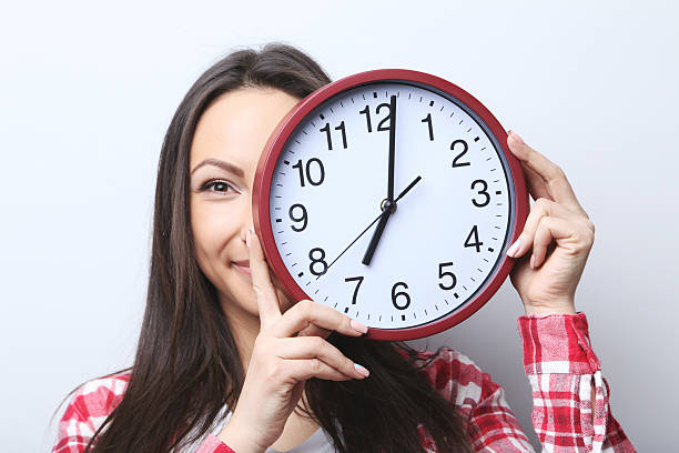 istock Young woman holding a clock on grey background 2205573031