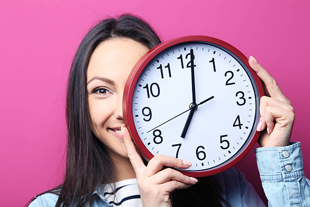 istock Young woman holding a clock on pink background 2205573168