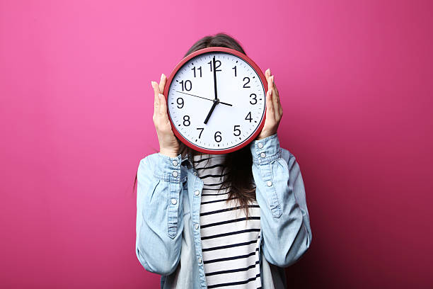 istock Young woman holding a clock on pink background 2205573933