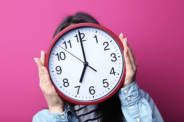 istock Young woman holding a clock on pink background 2205574422