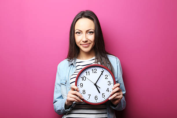 istock Young woman holding a clock on pink background 2205575793