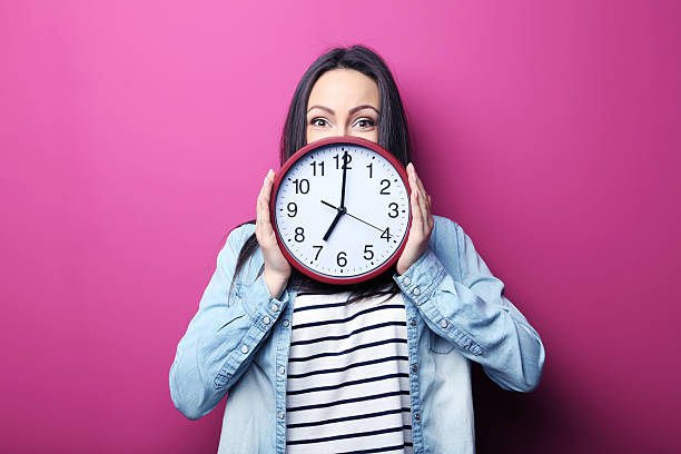 istock Young woman holding a clock on pink background 2205575923
