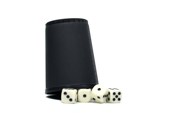 A studio shot of a game with a cup used for shaking dice, and the dice themselves scattered on a white surface ready for play.