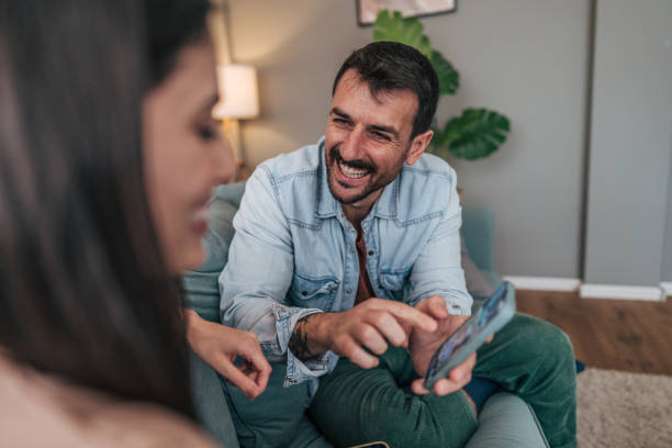 istock Couple relaxing on sofa, browsing smartphone together and laughing 2205577588