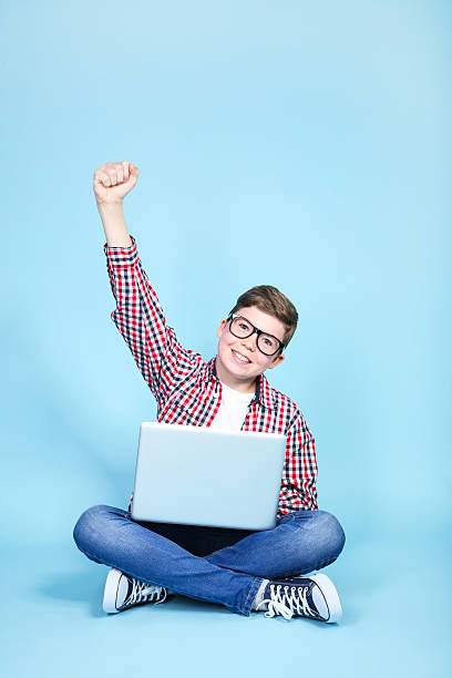 istock Young boy with a laptop sitting on blue background 2205580087