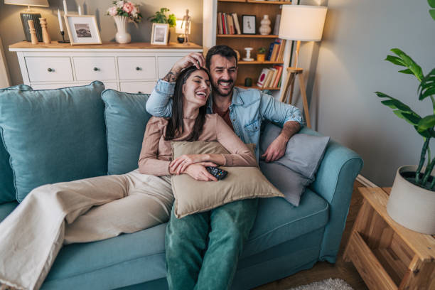 istock Young couple relaxing on sofa, watching television and laughing together 2205580250