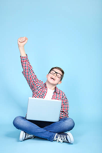 istock Young boy with a laptop sitting on blue background 2205580783