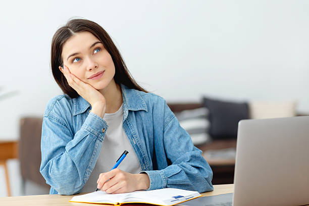 istock Young woman thinking and writing at home 2205581912