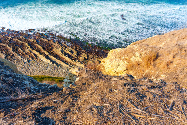 Vibrant coastal landscape featuring steep cliffs and rocky shorelines along the Pacific Ocean in Lunada Bay in Palos Verdes Estates, captured from a high vantage point under bright sunlight.