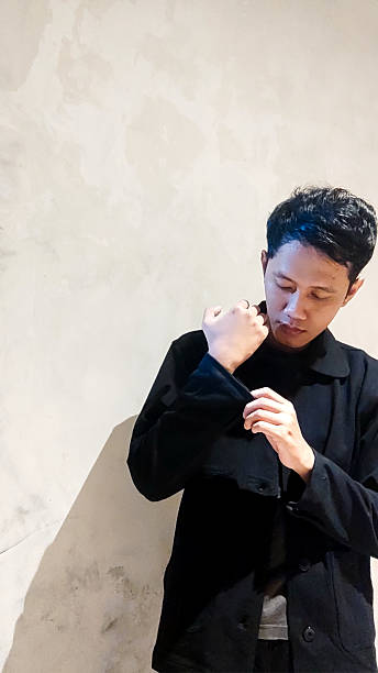 istock Young Man in Black Jacket Adjusting Sleeve Against Minimalist Wall 2205584017